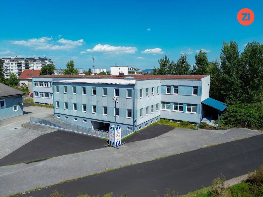 Außenansicht eines hellblauen Bürogebäudes mit vielen Fenstern und einem asphaltierten Parkplatz davor.