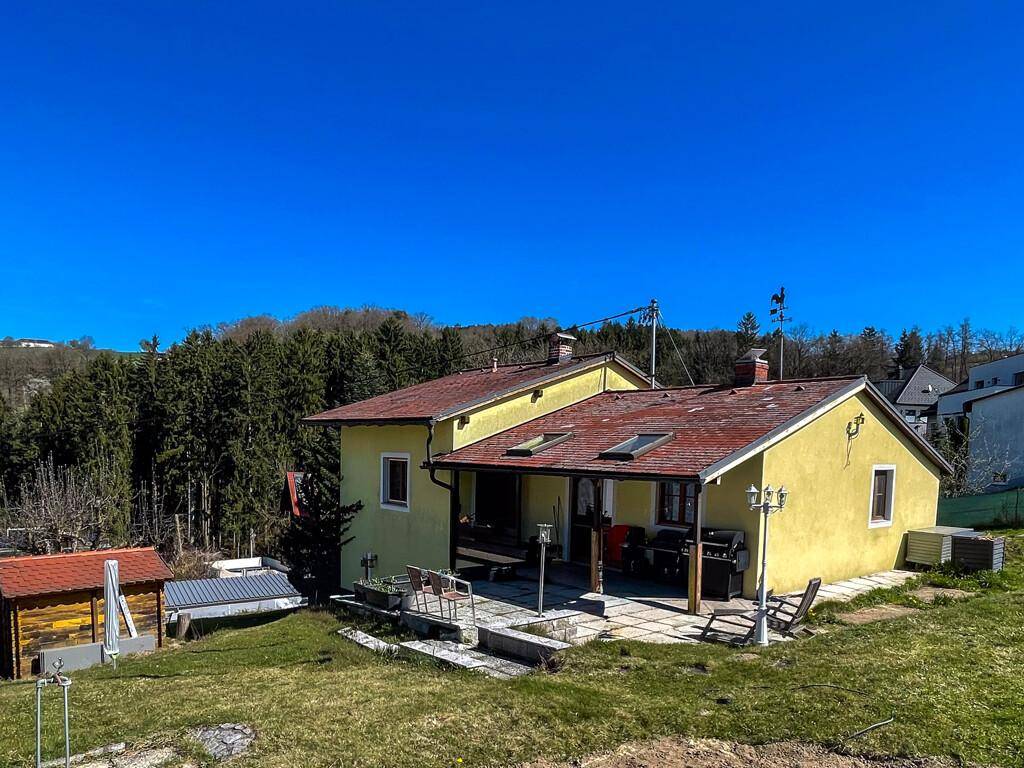 Rückseite des Hauses mit überdachter Terrasse, Grillbereich und Blick auf den Wald.