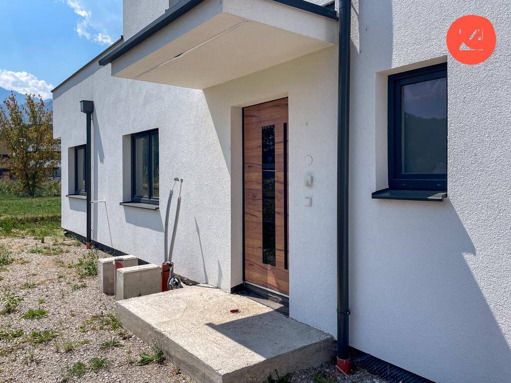 Moderner Hauseingang mit Holztür und Vordach an der weißen Fassade.