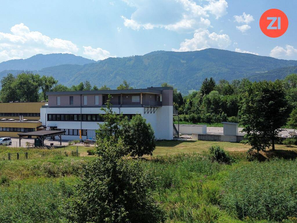 Weitläufige grüne Landschaft mit Bergen im Hintergrund und umliegenden Gebäuden.