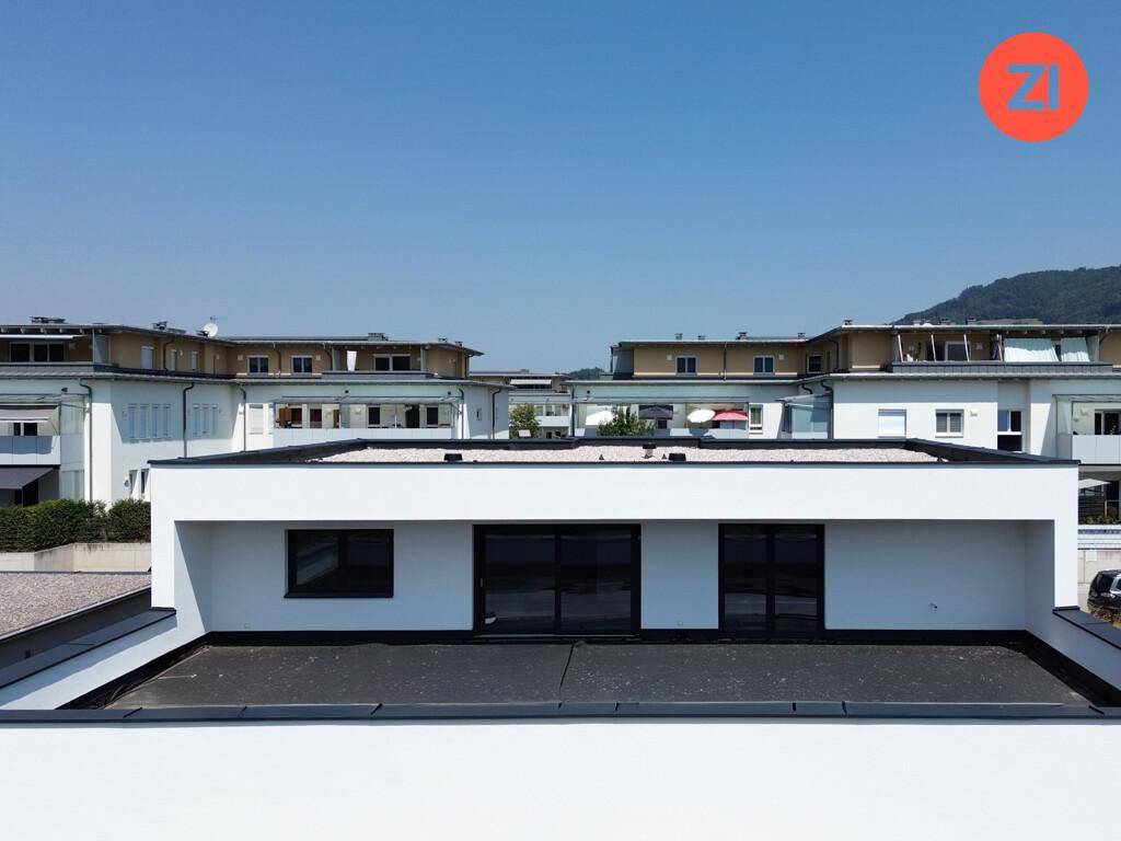 Obergeschoss eines modernen Gebäudes mit Flachdach und großen Fenstern, umgeben von anderen Gebäuden.