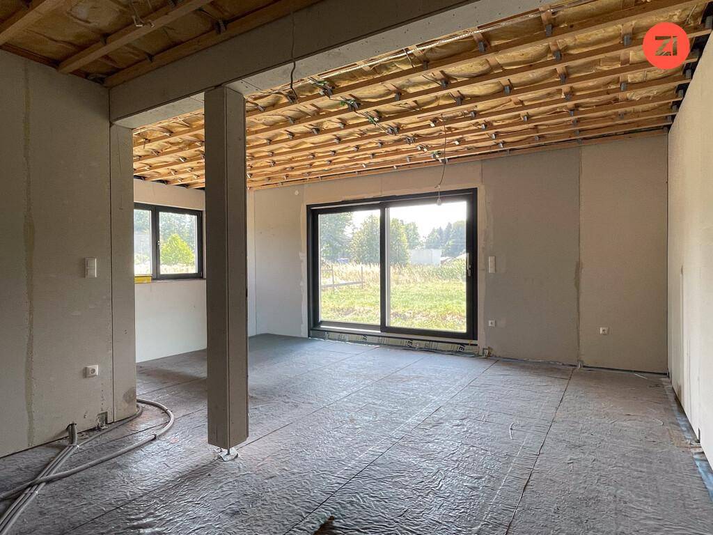 Geräumiger Wohnbereich im Rohbau mit großen Fenstern und Blick ins Grüne.