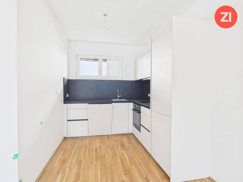 Moderne, kompakte Küche mit weißen Schränken, dunkler Arbeitsplatte und einem Fenster für Tageslicht.