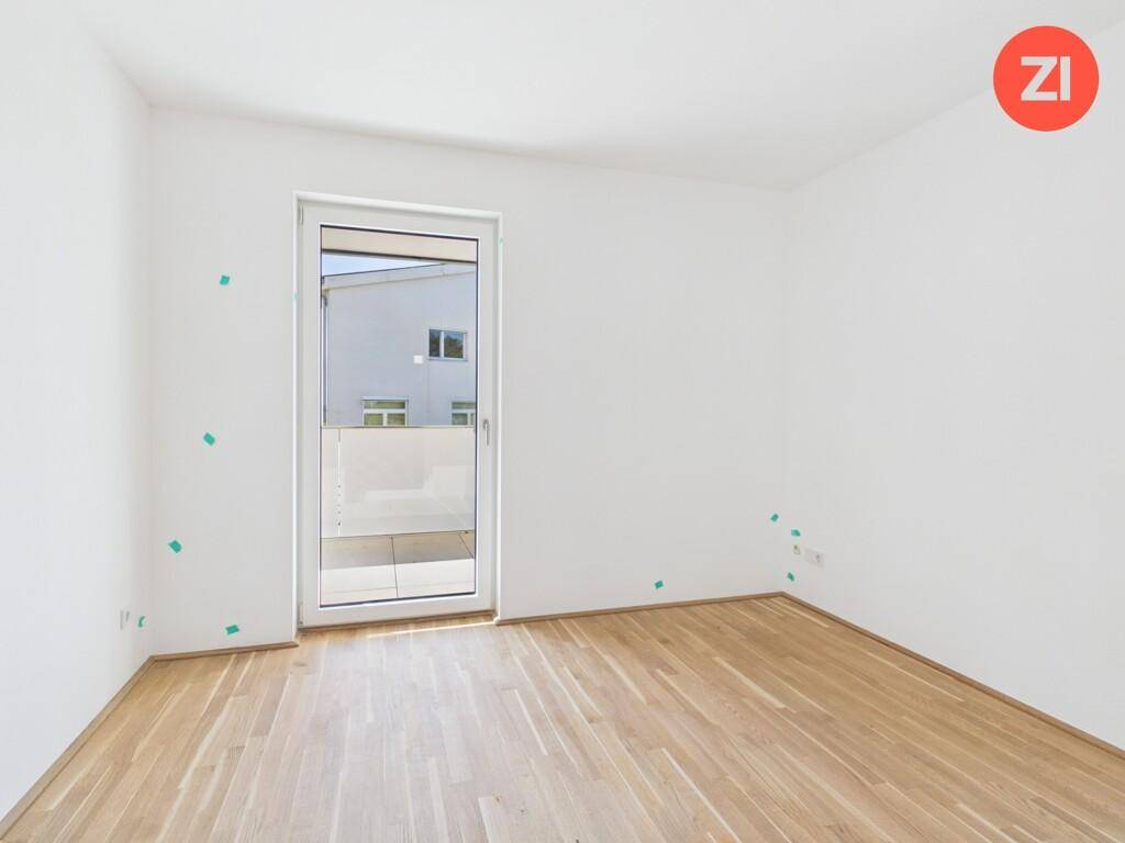 Helles, leeres Zimmer mit Parkettboden und Zugang zu einem Außenbereich durch eine Glastür.