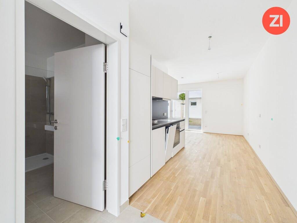 Offener Wohnbereich mit Küchenzeile, Zugang zum Garten und Blick ins Badezimmer.