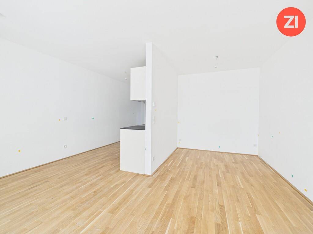 Geräumiger, leerer Wohnbereich mit hellem Holzfußboden und weißen Wänden.