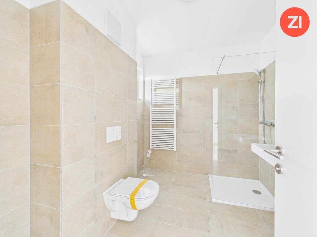Modernes Badezimmer mit beigefarbenen Fliesen, ebenerdiger Dusche und Wand-WC.