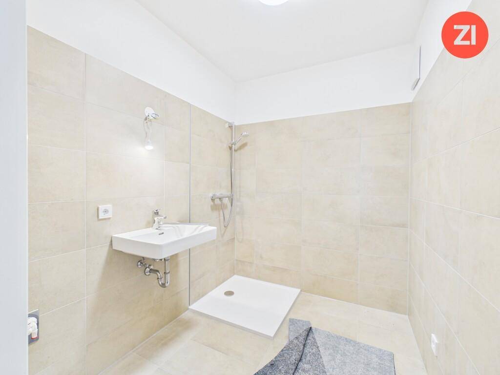 Modernes Badezimmer mit beigefarbenen Fliesen, wandhängendem Waschbecken und ebenerdiger Dusche.