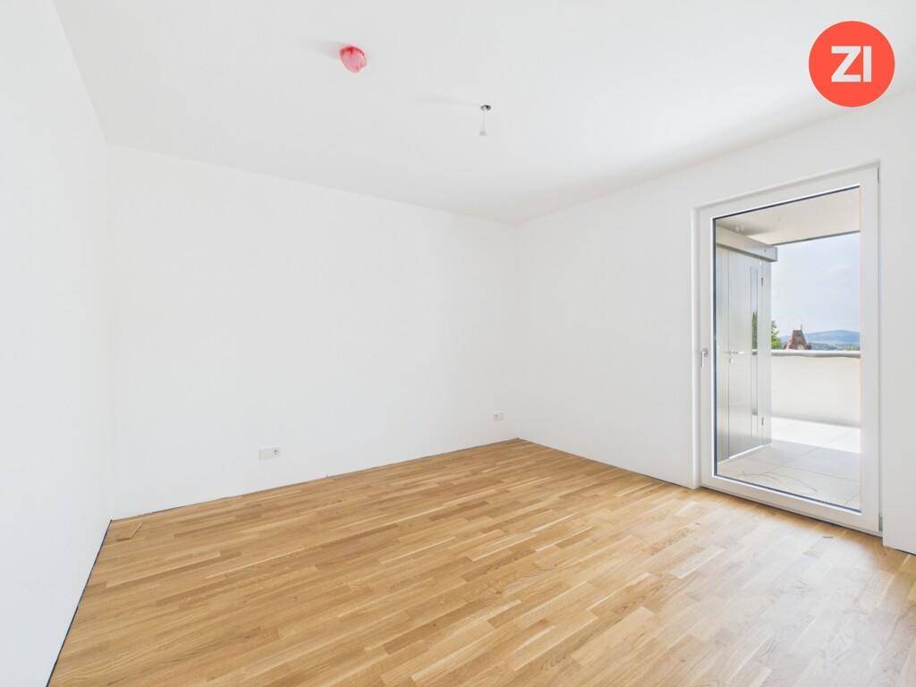 Leeres Schlafzimmer mit hellem Parkettboden und direktem Zugang zu einem Balkon.