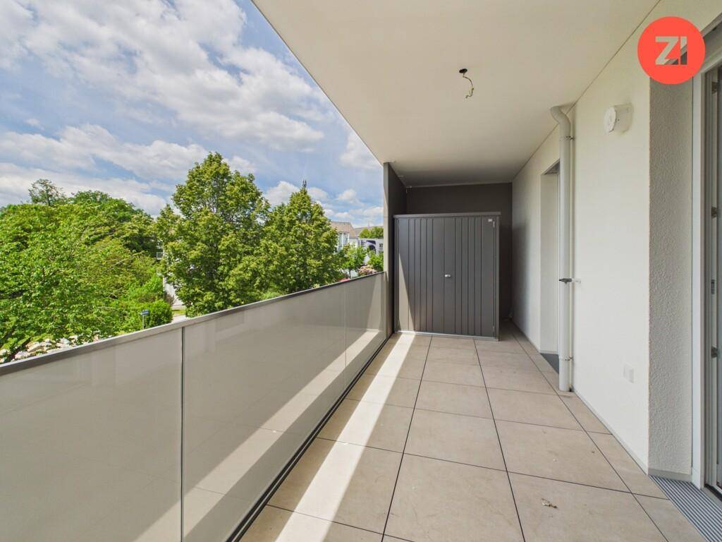 Geräumiger Balkon mit Fliesenboden und integriertem Abstellschrank, umgeben von Grün.