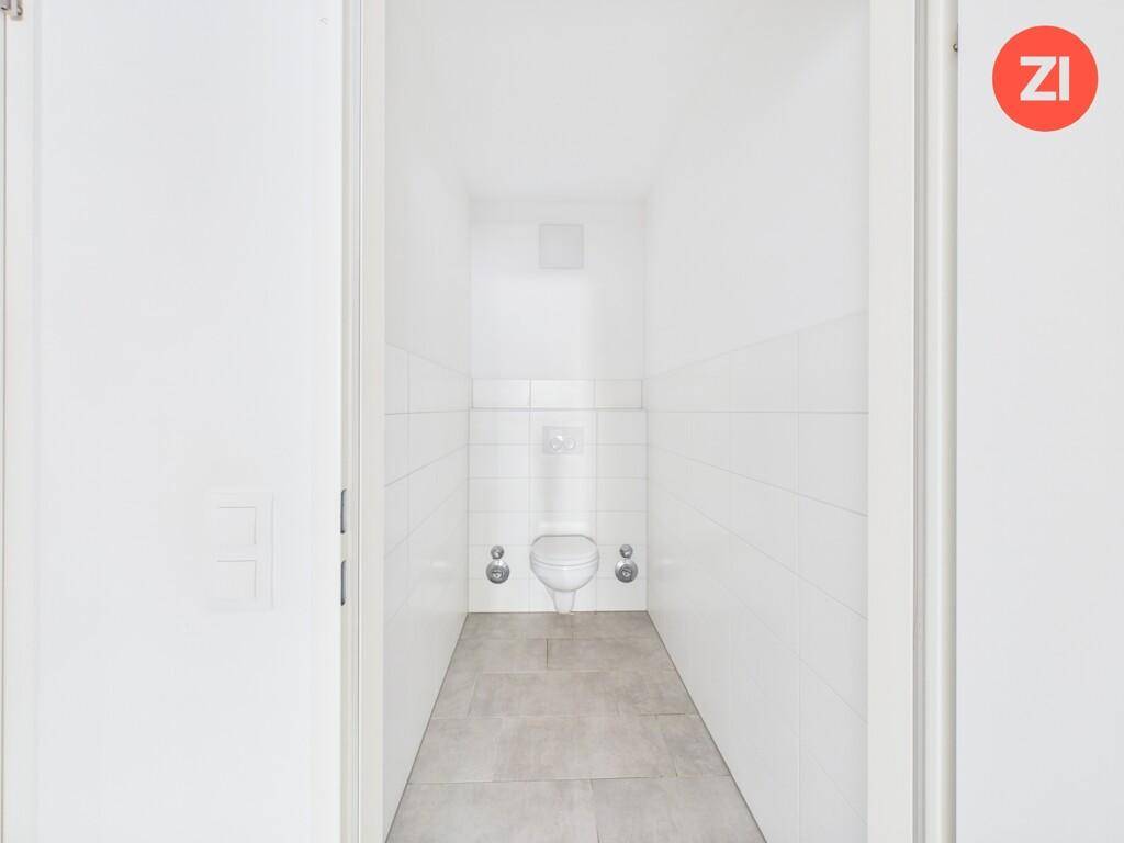 Separates WC mit wandmontierter Toilette und hellen Fliesen an Wänden und Boden.