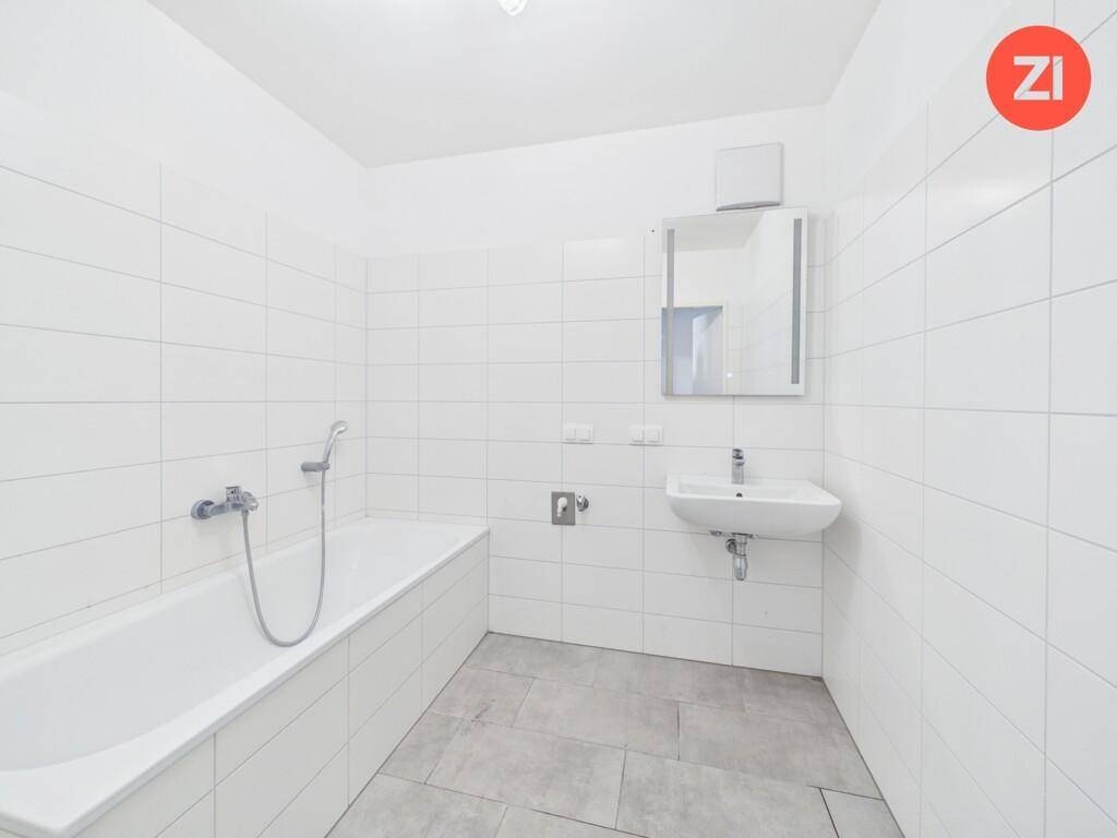 Modernes Badezimmer mit Badewanne, Waschbecken und weißen Fliesen an Wänden und Boden.