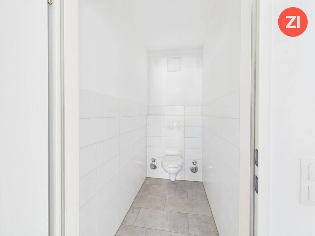 Separates WC mit weißen Wandfliesen, wandhängender Toilette und Fliesenboden.