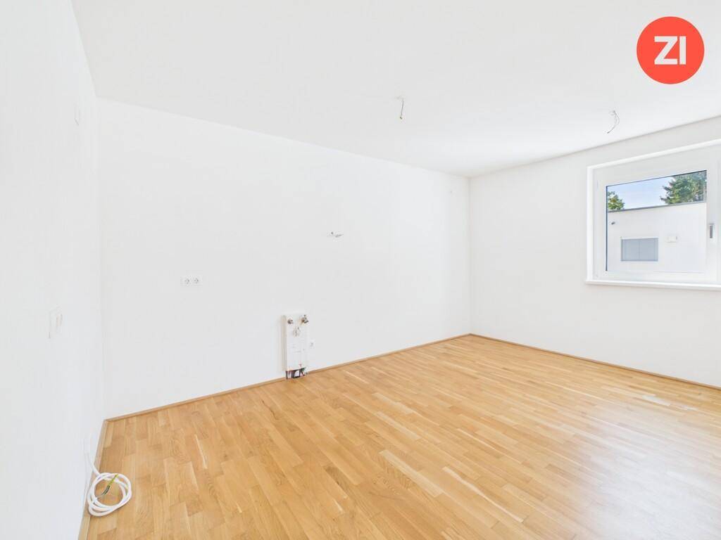 Helles Zimmer mit Parkettboden und einem Fenster, das viel Tageslicht hereinlässt.