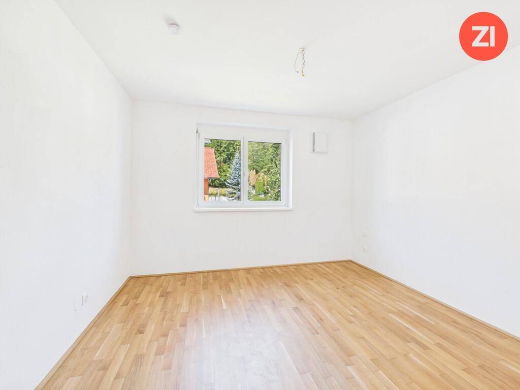 Helles Zimmer mit Parkettboden und einem Fenster mit Blick ins Grüne.