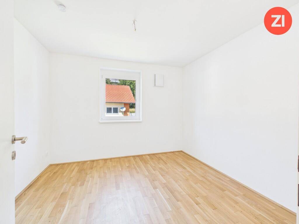 Helles Schlafzimmer mit Parkettboden und einem Fenster mit Blick auf die Nachbarschaft.