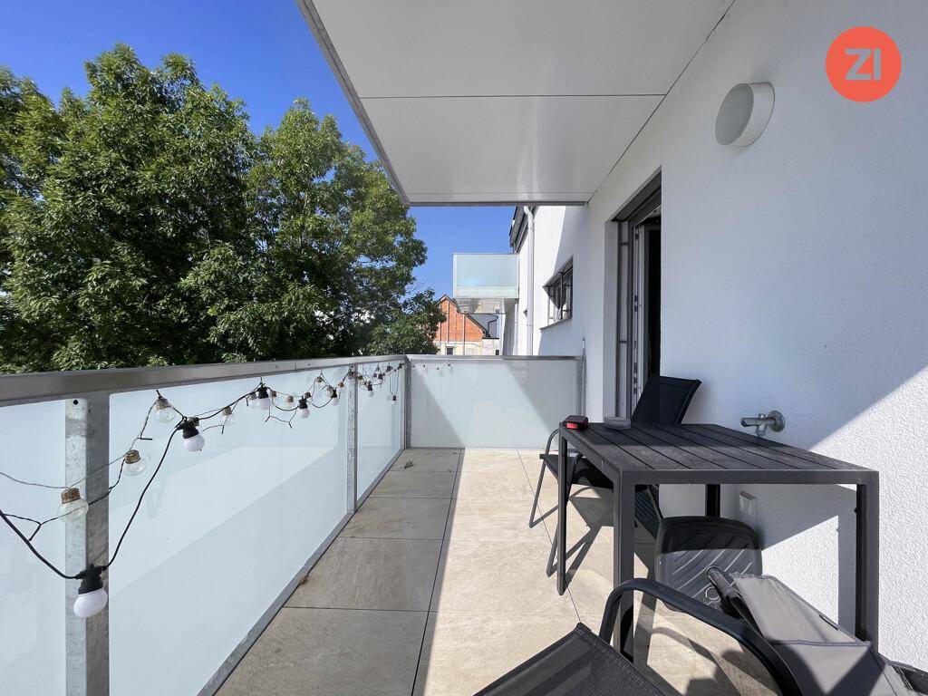 Geräumiger Balkon mit Glasbrüstung, Sitzgelegenheiten und Blick ins Grüne.