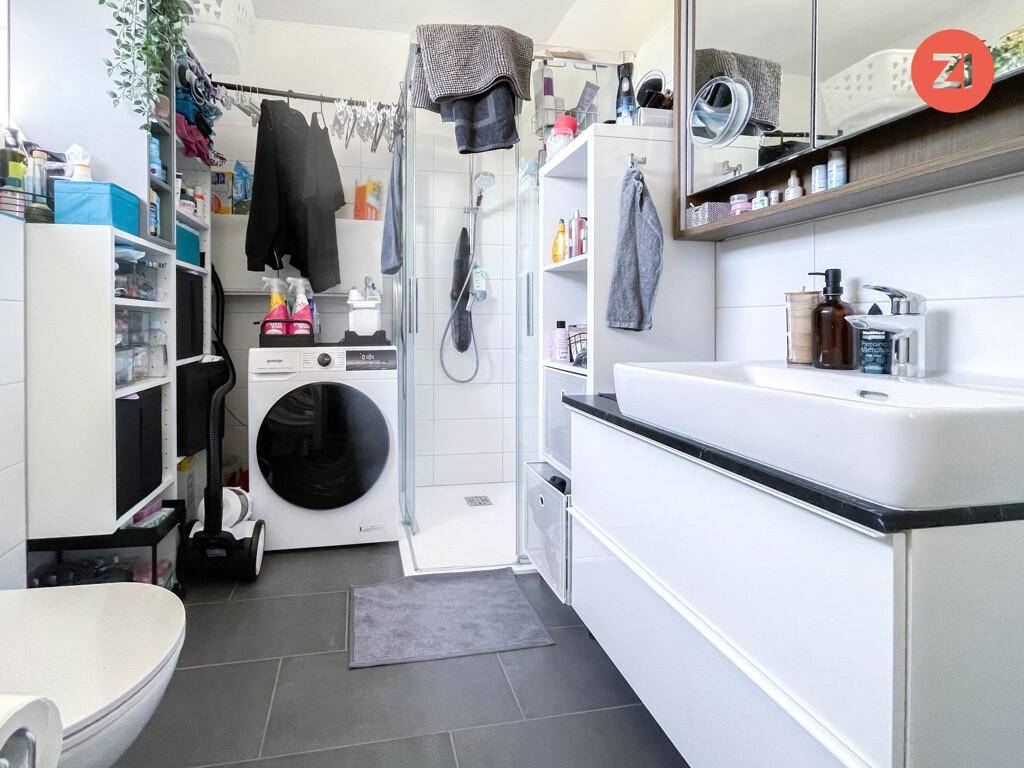 Modernes Badezimmer mit Dusche, Waschmaschine, Einzelwaschbecken und dunklen Fliesen.