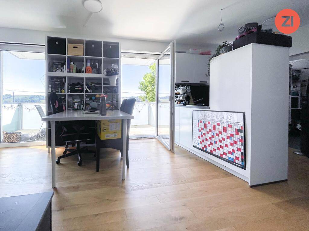 Heller Wohnbereich mit Holzboden, Arbeitsplatz und Zugang zu einem großen Balkon.