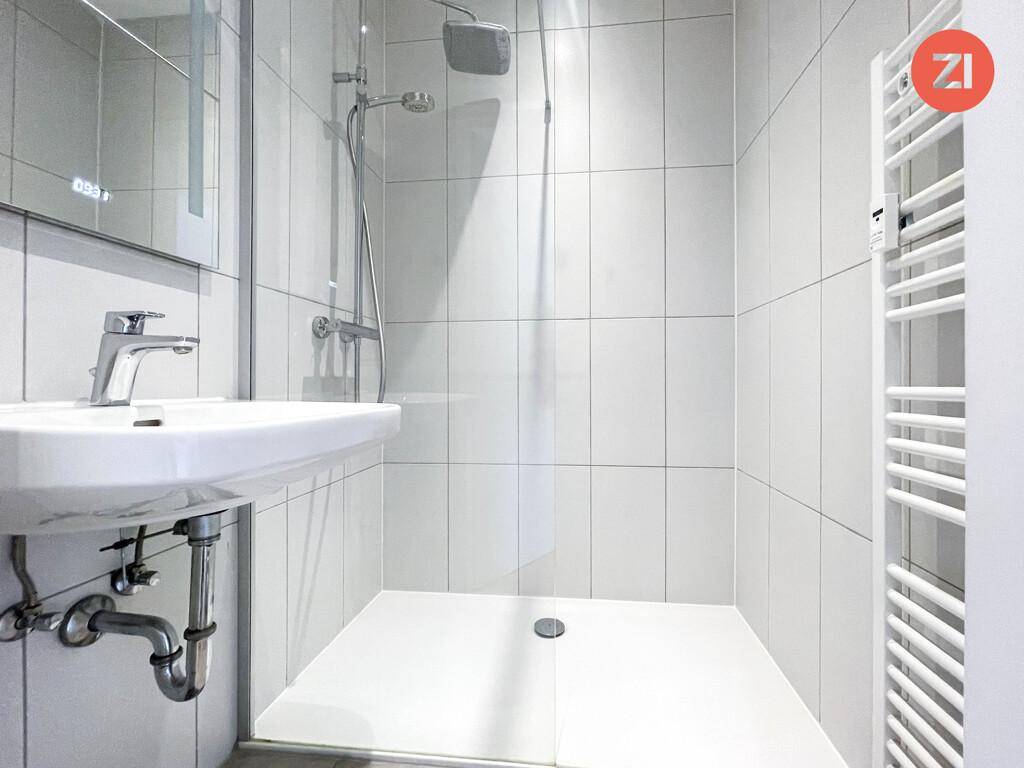 Modernes Badezimmer mit weißen Fliesen, Dusche, Waschbecken und beheiztem Handtuchhalter.