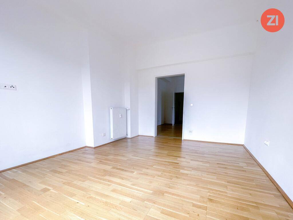 Leerer Raum mit Parkettboden, weißen Wänden und Heizkörper, bietet vielseitige Nutzungsmöglichkeiten.