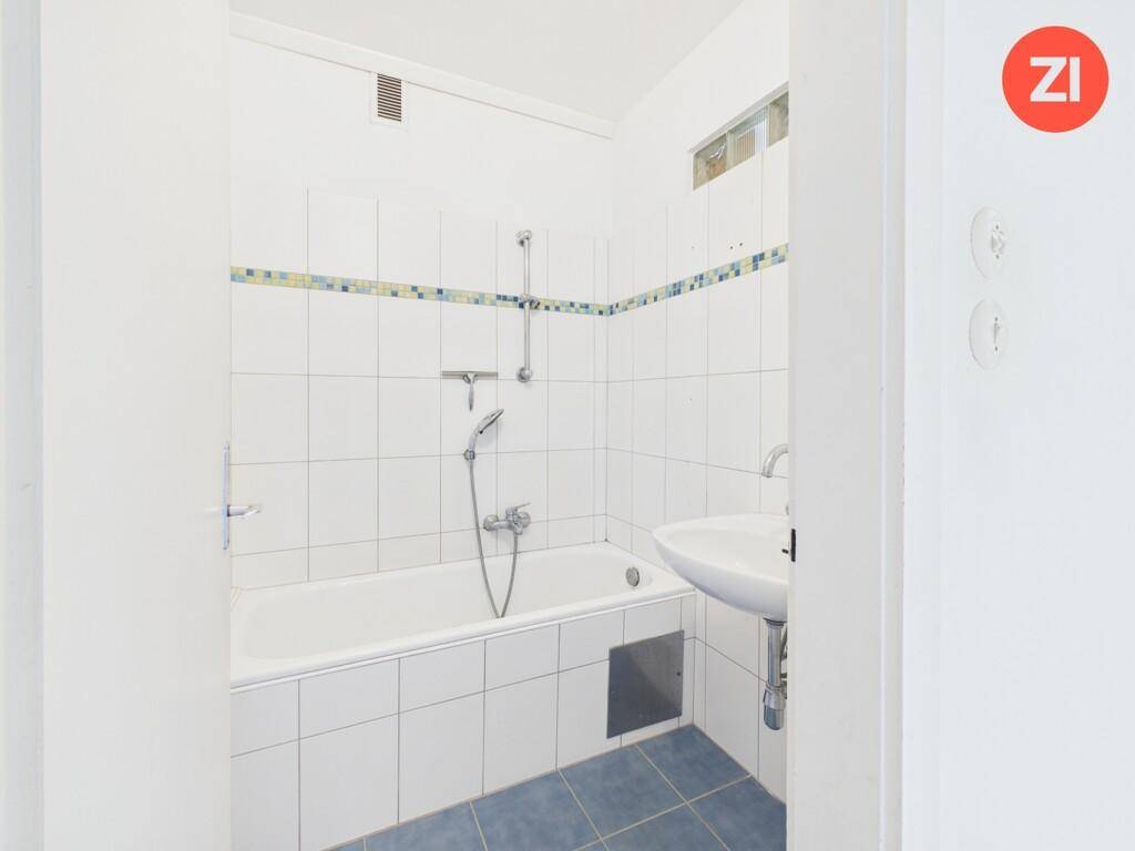 Badezimmer mit Badewanne, Waschbecken und weißen Fliesen mit blauer Bordüre.