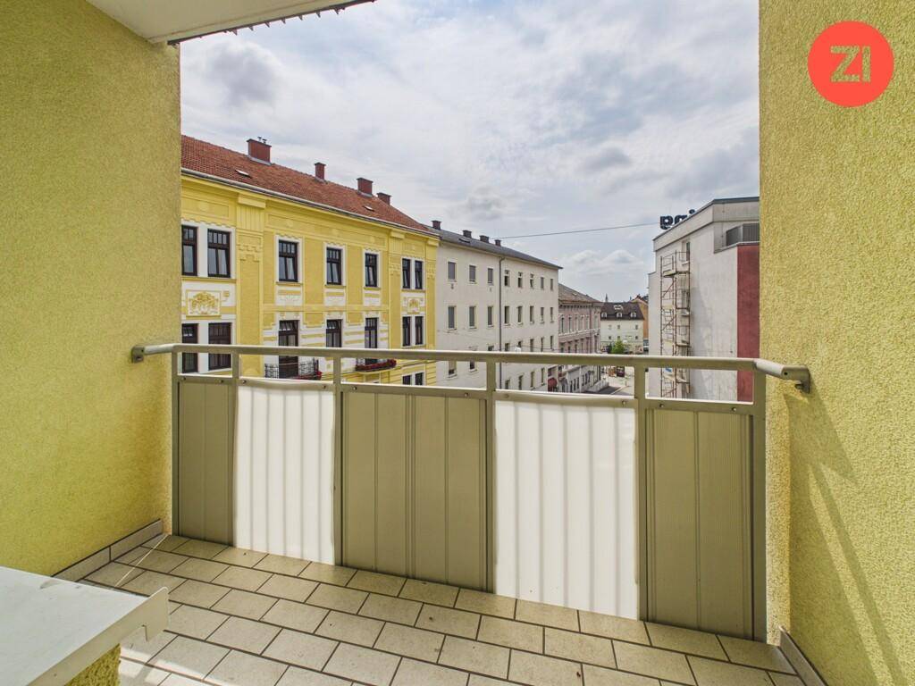 Kleiner Balkon mit Fliesenboden und Blick auf die umliegenden Gebäude der Stadt.