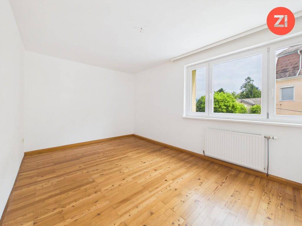 Helles, leeres Schlafzimmer mit Holzboden und großem Fenster mit Blick nach draußen.