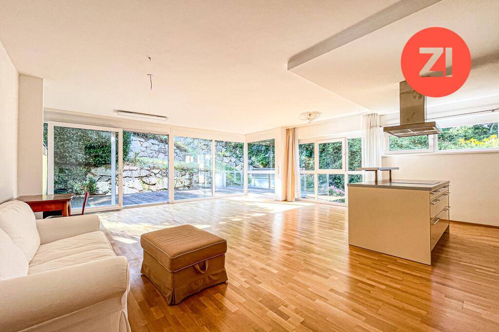 Geräumiger Wohnbereich mit bequemer Couch, Kücheninsel und viel Tageslicht durch die großen Fenster zum Garten.