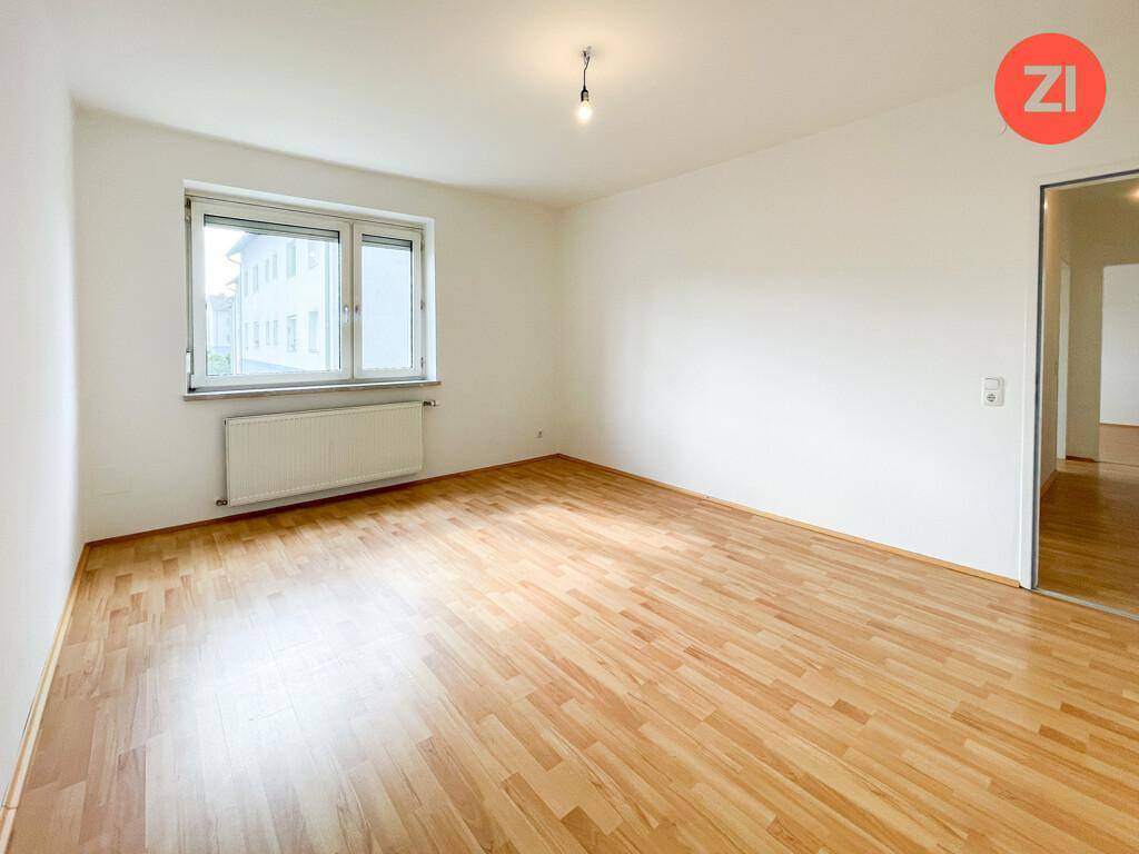Geräumiges Zimmer mit hellem Parkettboden und Zugang zu einem weiteren Raum durch eine Glastür.