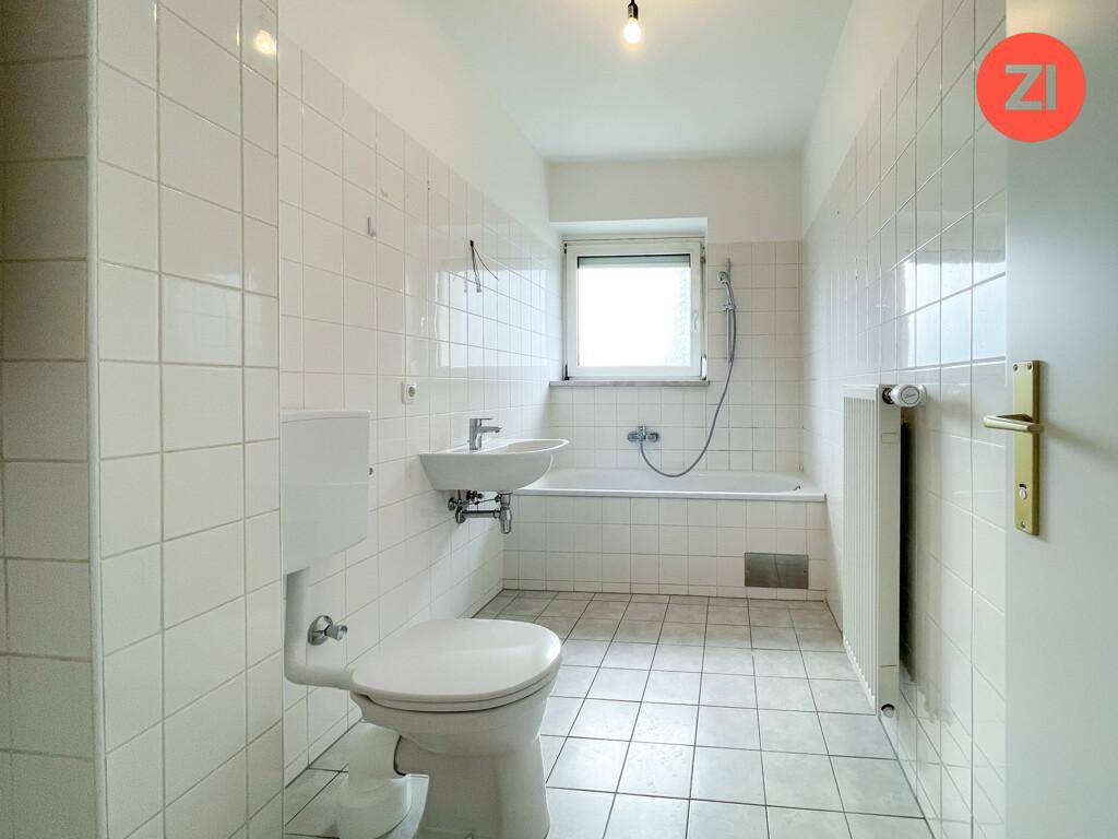 Funktionales Badezimmer mit weißen Fliesen, Badewanne, WC, Waschbecken und einem Fenster.