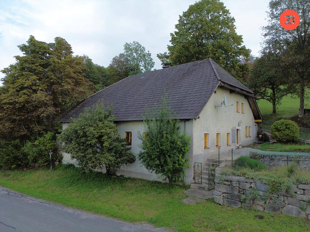 Ländliches Wohnhaus mit traditioneller Architektur, umgeben von Bäumen und grüner Landschaft.