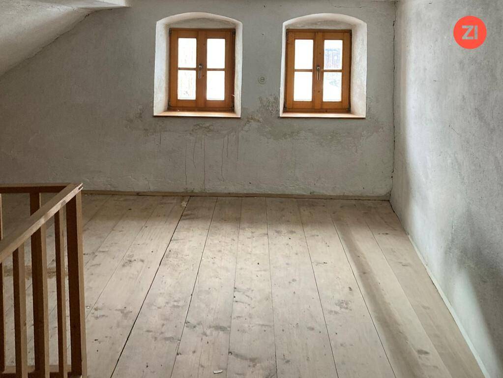 Unausgebauter Dachbodenraum mit Holzdielenboden und zwei kleinen, traditionellen Fenstern.