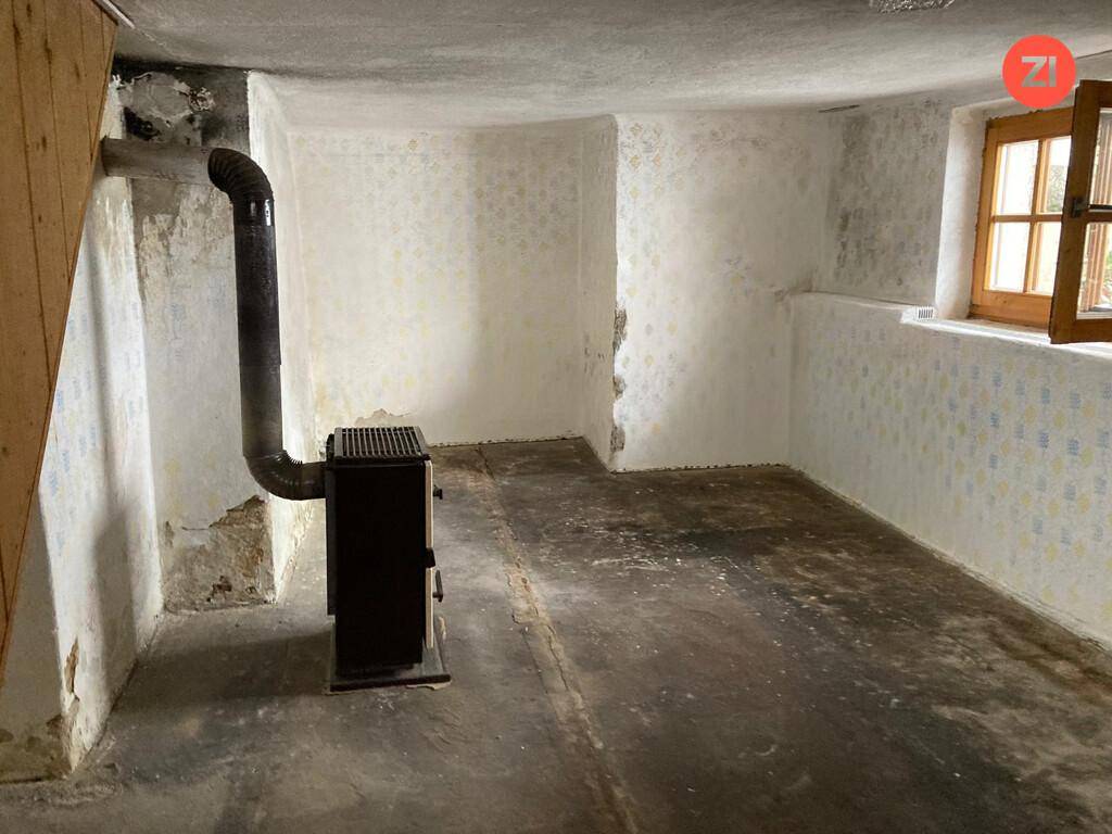 Einfacher Kellerraum mit Betonboden, einem Holzofen und einem kleinen Fenster.