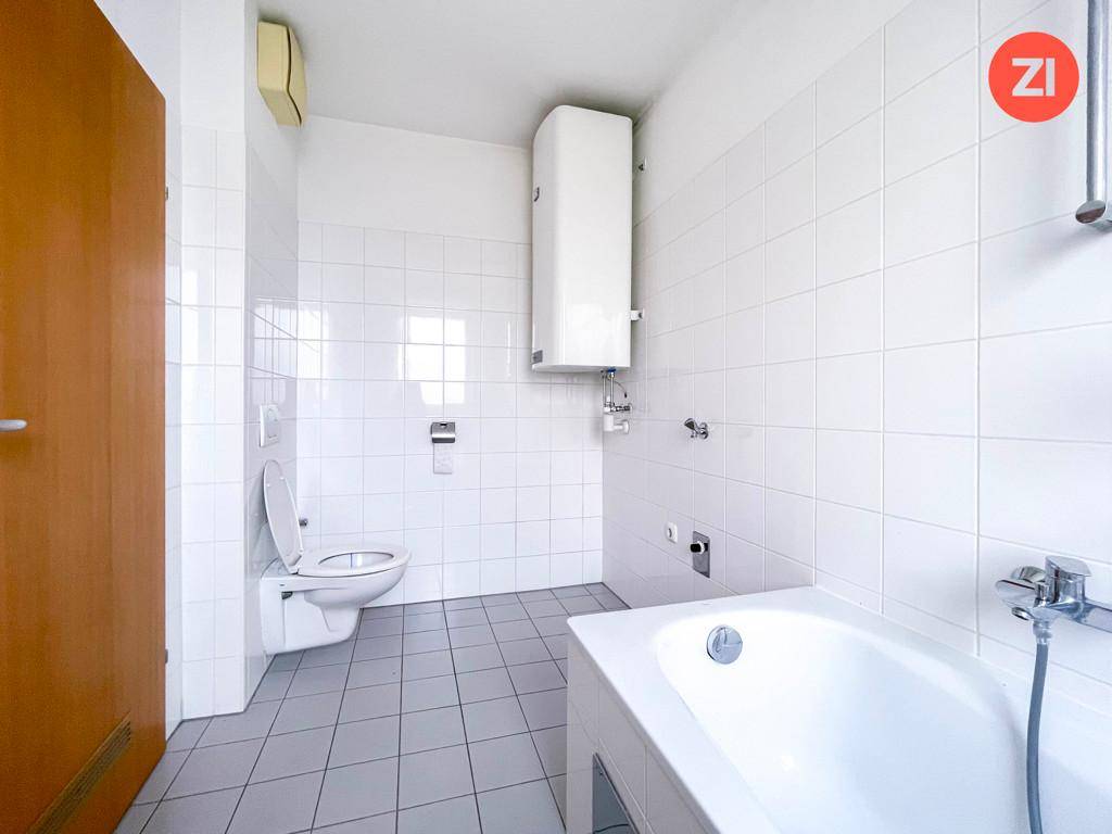 Funktionales Badezimmer mit weißen Wandfliesen, grauen Bodenfliesen, Badewanne und Toilette.