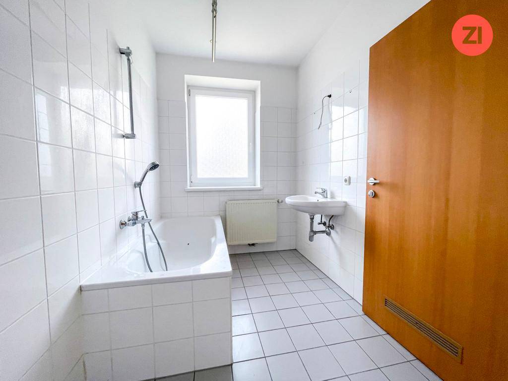 Helles Badezimmer mit Badewanne, Duschfunktion, Waschbecken und Fenster für Tageslicht.