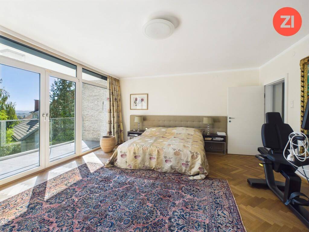 Helles Schlafzimmer mit Parkettboden, großem Fenster und Zugang zu einem Balkon.