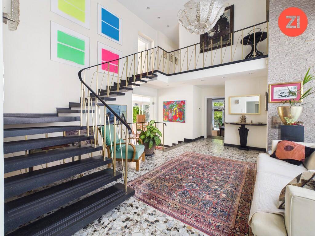 Großzügiger Eingangsbereich mit eleganter Treppe, Kunstwerken und Terrazzoboden.