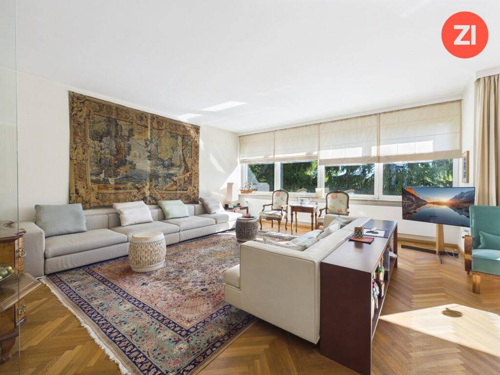 Gemütlicher Wohnbereich mit großem Sofa, Teppich und Blick ins Grüne durch breite Fenster.