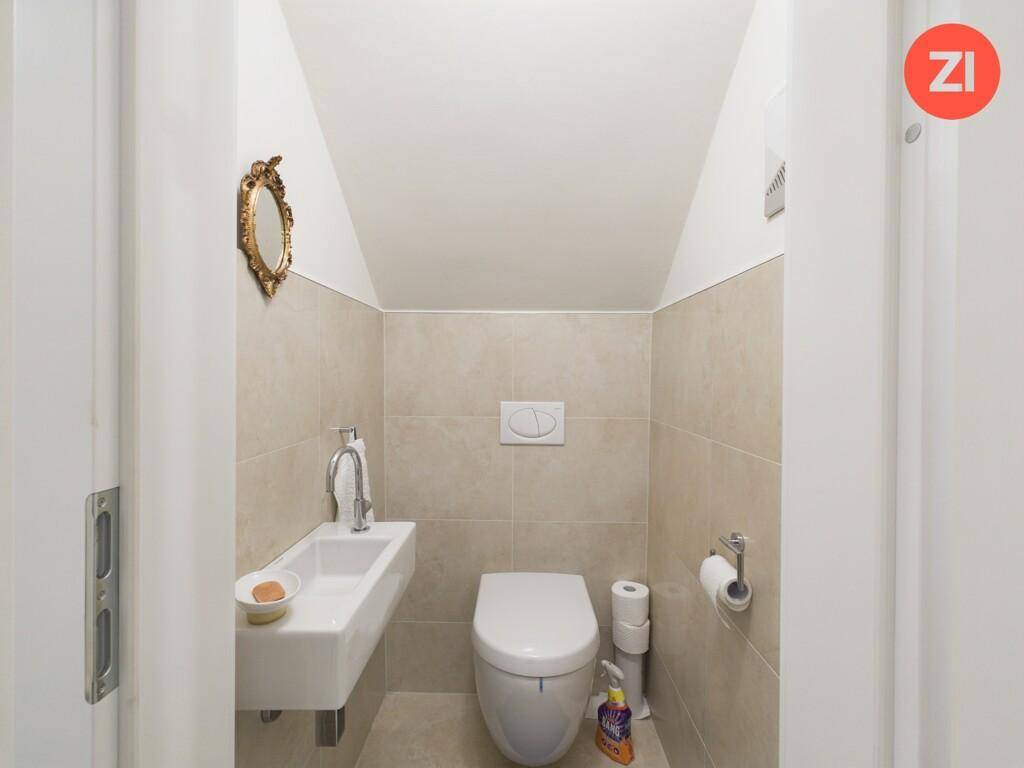 Kleines Gäste-WC mit Wand-WC, Waschbecken und hellen Fliesen.