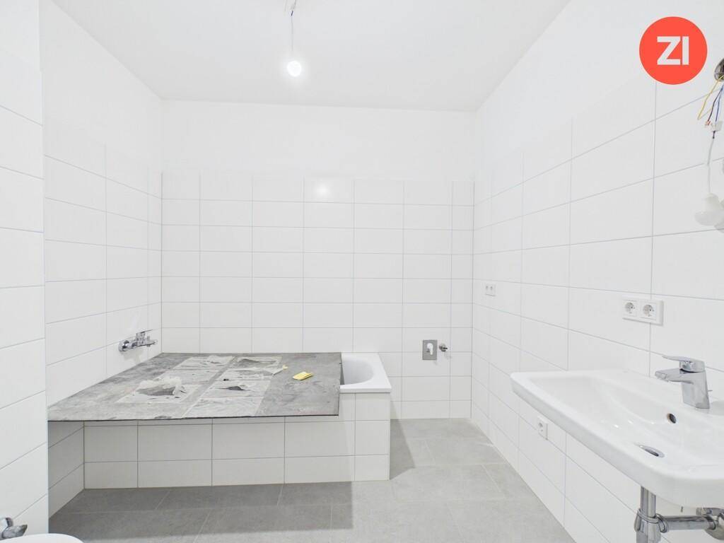 Modernes Badezimmer im Bau mit weißen Fliesen, Badewanne und Waschbecken.