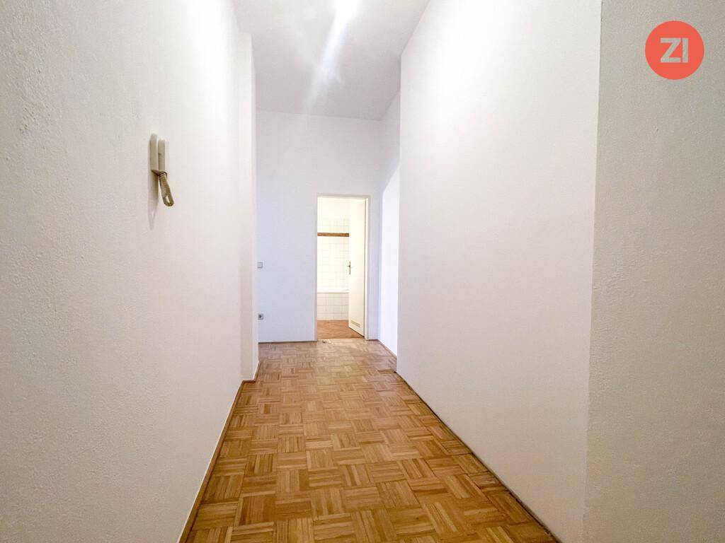 Langer Flur mit Parkettboden, weißen Wänden und Zugang zu weiteren Räumen der Wohnung.