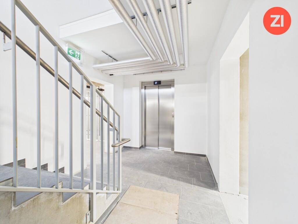 Treppenhaus und moderner Aufzug in einem Mehrfamilienhaus mit sichtbaren Leitungen.
