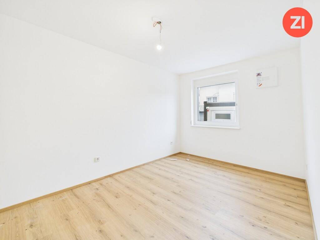 Leeres Zimmer mit Laminatboden, weißen Wänden und einem Fenster für natürliches Licht.