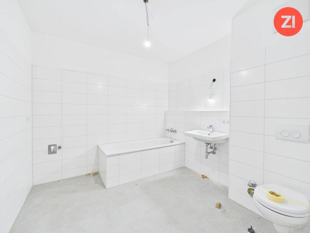 Unfertiges Badezimmer mit weißen Fliesen, Badewanne und Waschbecken, bereit für den Ausbau.
