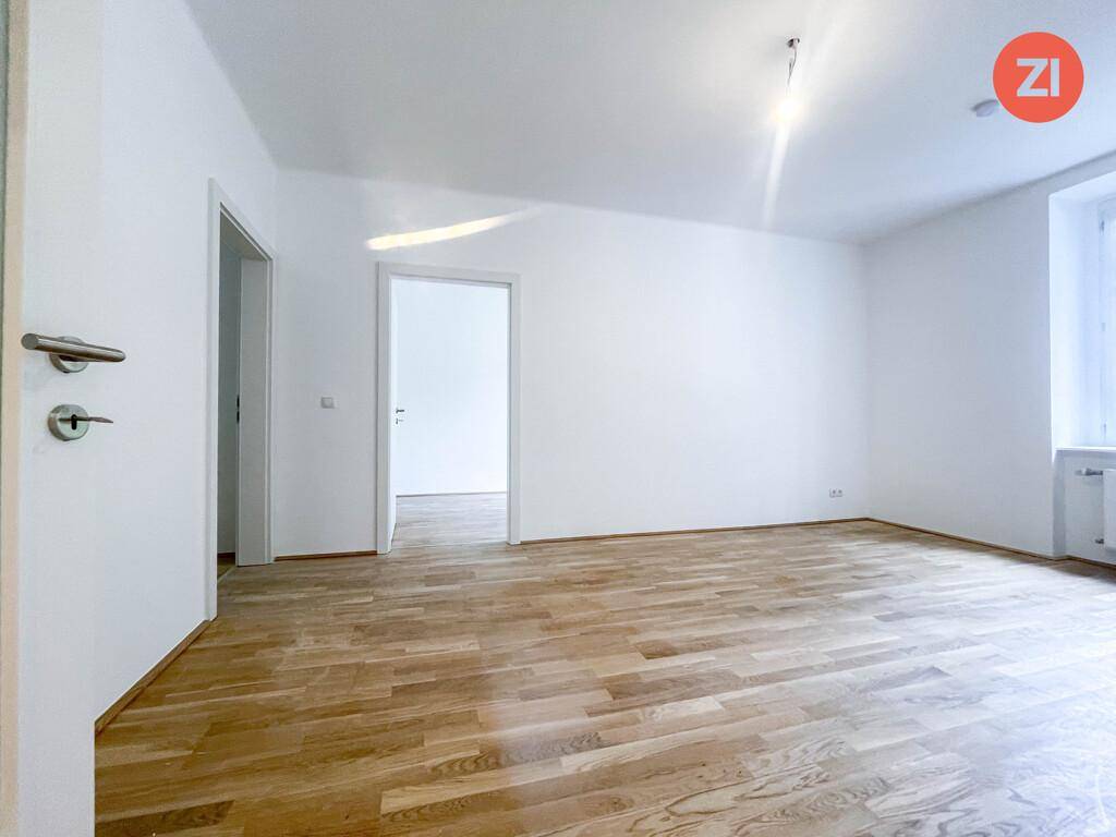 Leerer, heller Raum mit Holzparkettboden und zwei Türen, bereit zur individuellen Gestaltung.
