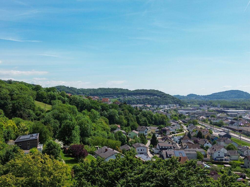 Panoramablick auf eine Wohnsiedlung in einer hügeligen, grünen Landschaft mit Fernsicht.