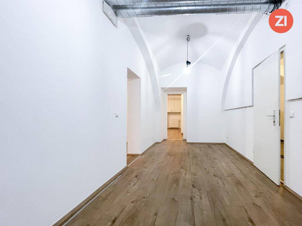 Heller Raum mit Holzboden, weißen Wänden, Gewölbedecke und Durchgängen zu weiteren Zimmern.