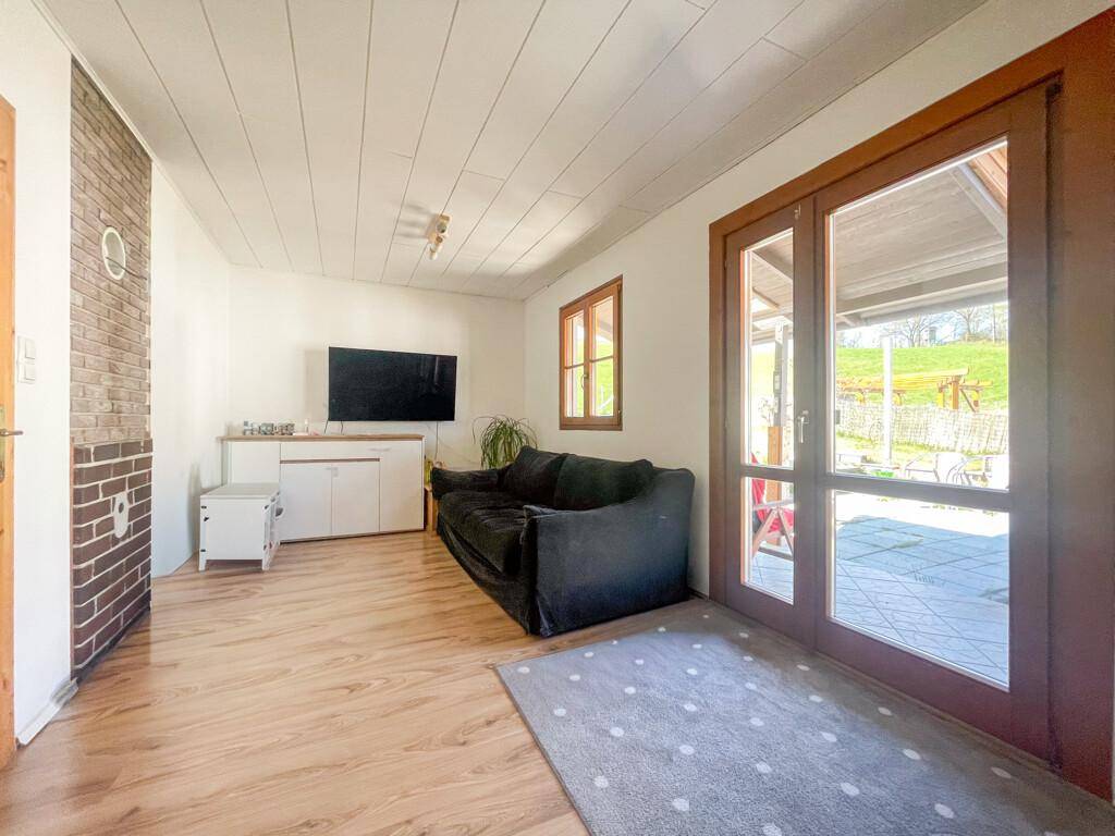 Helles Wohnzimmer mit Laminatboden, Ziegelwandakzent und direktem Zugang zur Terrasse.