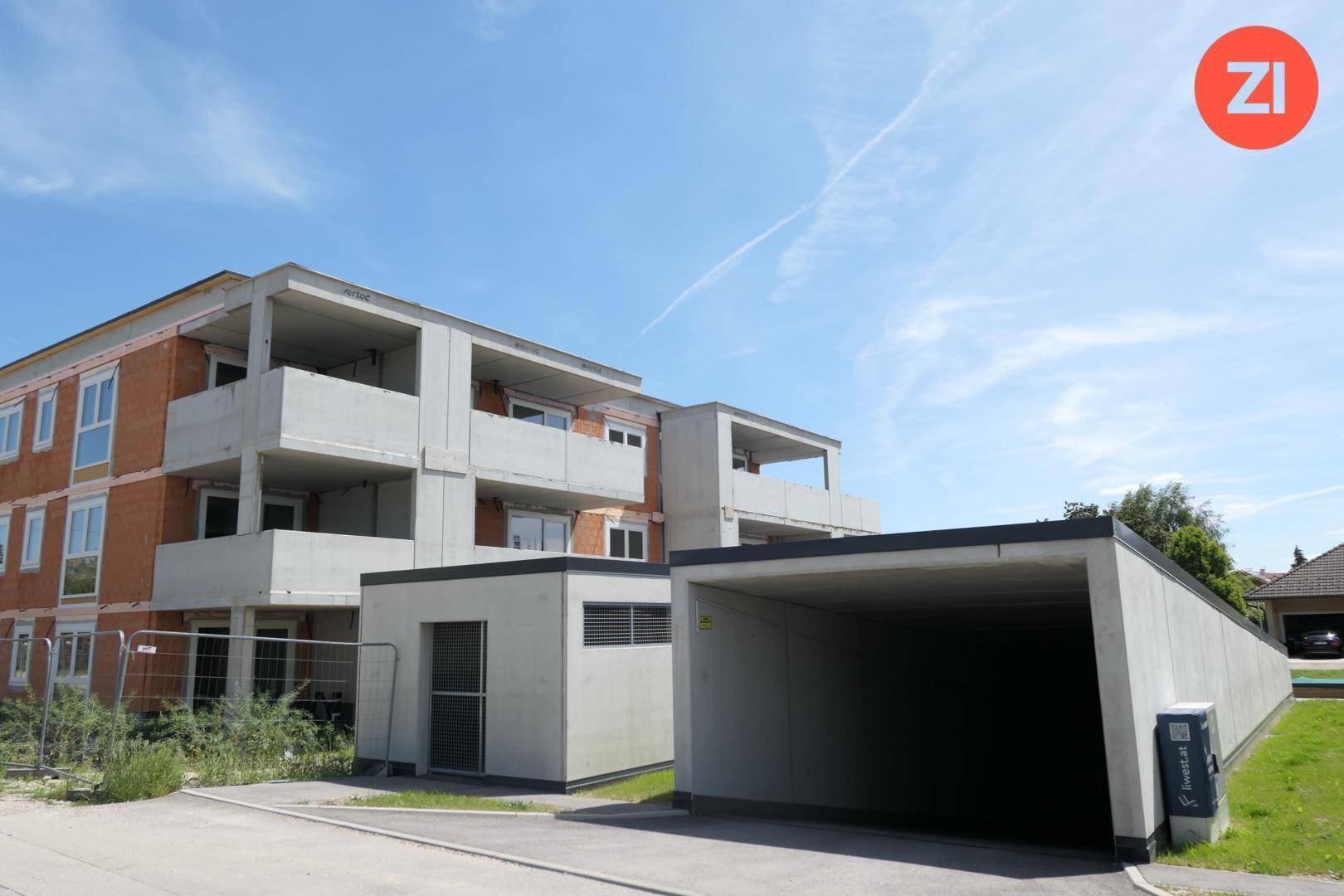 Neubau-Mehrfamilienhaus mit Tiefgaragenzufahrt und moderner Architektur unter blauem Himmel.
